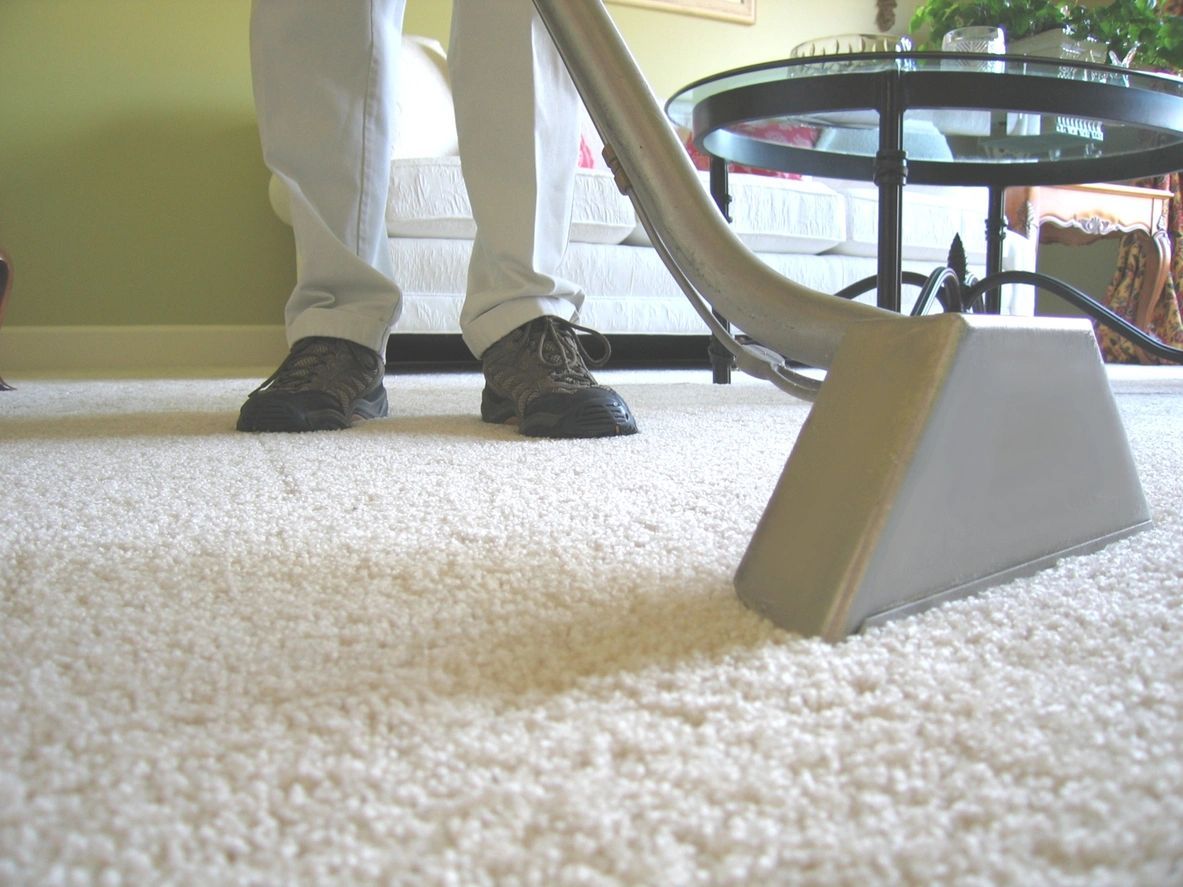 A person is using a vacuum cleaner on a white carpet