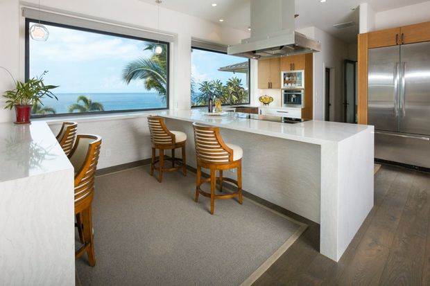 Modern kitchen with ocean view, white countertops, wooden bar stools, stainless steel appliances.