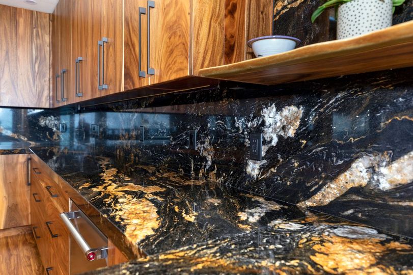 Black granite countertop with gold and white veining, against wooden cabinets.