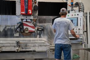Man operating stone-cutting machine in a workshop. Machine has American flag design on blade.