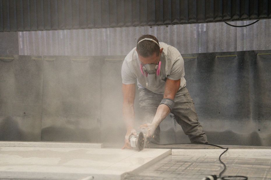 Man using a grinder, covered in dust, wearing a mask in a workshop.