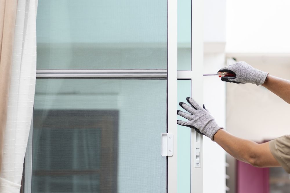 A person is opening a sliding glass door with a screwdriver.