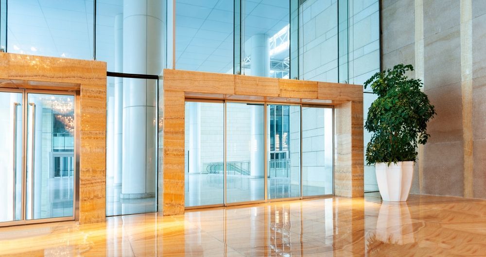 An empty lobby of a large building with sliding glass doors and a potted plant.