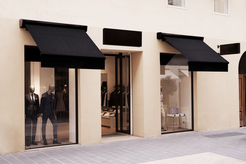 A store front with black awnings and mannequins in the window