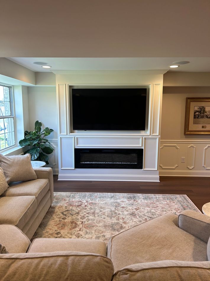 Basement with mounted TV, fireplace, beige sofas, and patterned rug