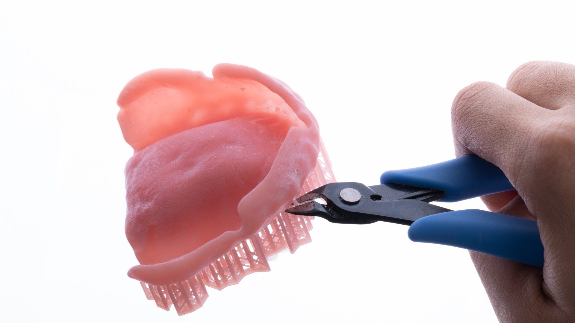 A person is holding a pair of pliers over a denture.