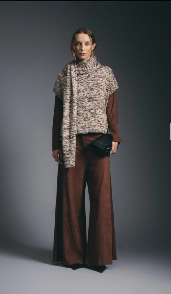 Modelo de moda con chaleco de piel texturizada y pantalones anchos marrones sobre un fondo de estudio gris.
