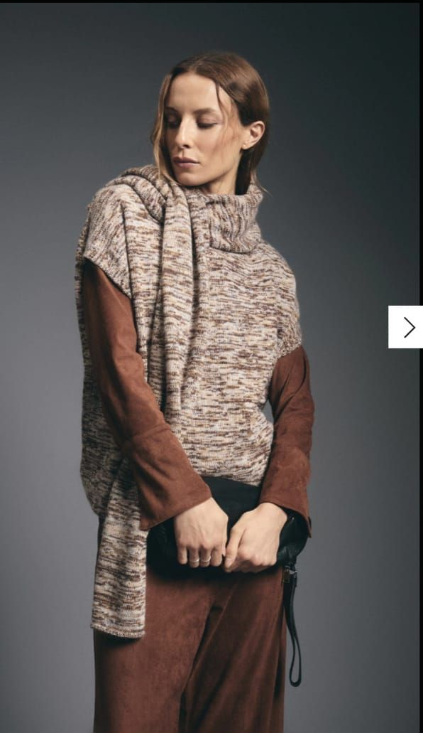 Modelo de moda con chaleco de piel texturizada y pantalones anchos marrones sobre un fondo de estudio gris.