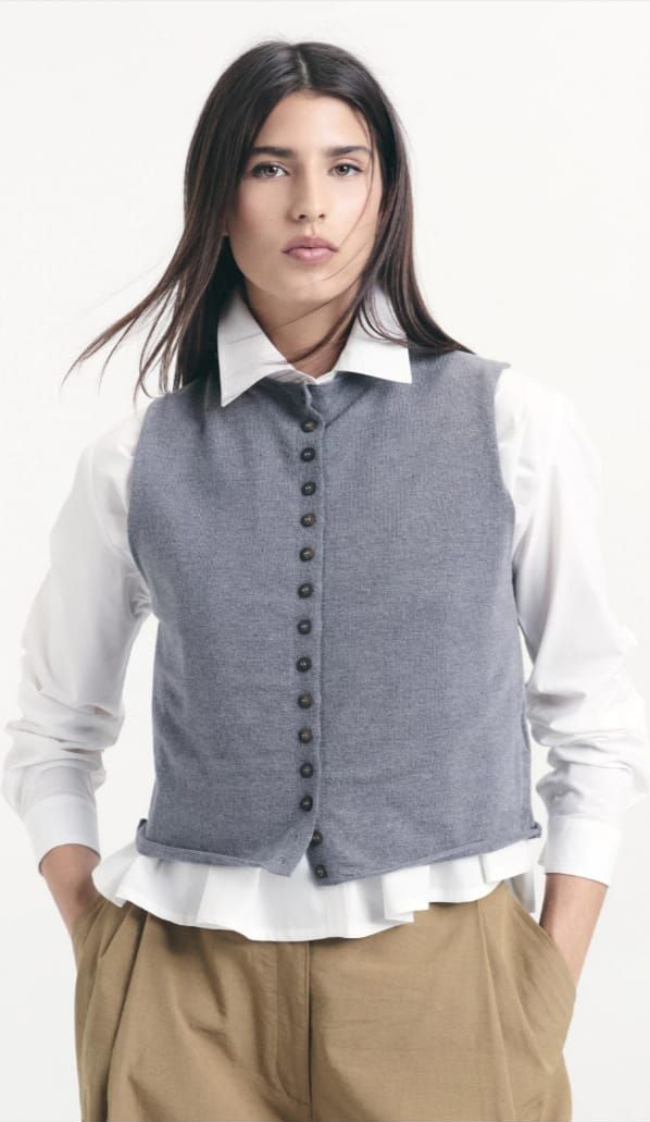 Mujer con blusa gris y pantalones anchos color canela, de pie sobre un fondo blanco.