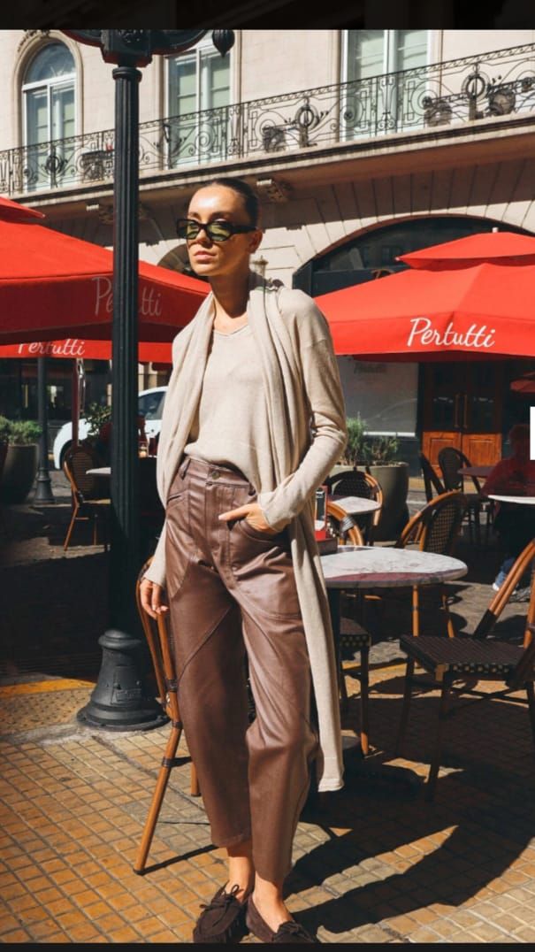 Mujer con vestido de rayas y abrigo beige de pie en una acera de la ciudad frente a un edificio clásico.