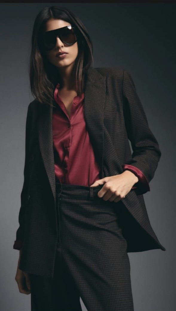 Persona con gafas de sol, traje oscuro de raya diplomática y camisa roja, sobre un fondo oscuro.