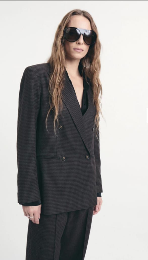 Persona con gafas de sol, traje oscuro de raya diplomática y camisa roja, sobre un fondo oscuro.