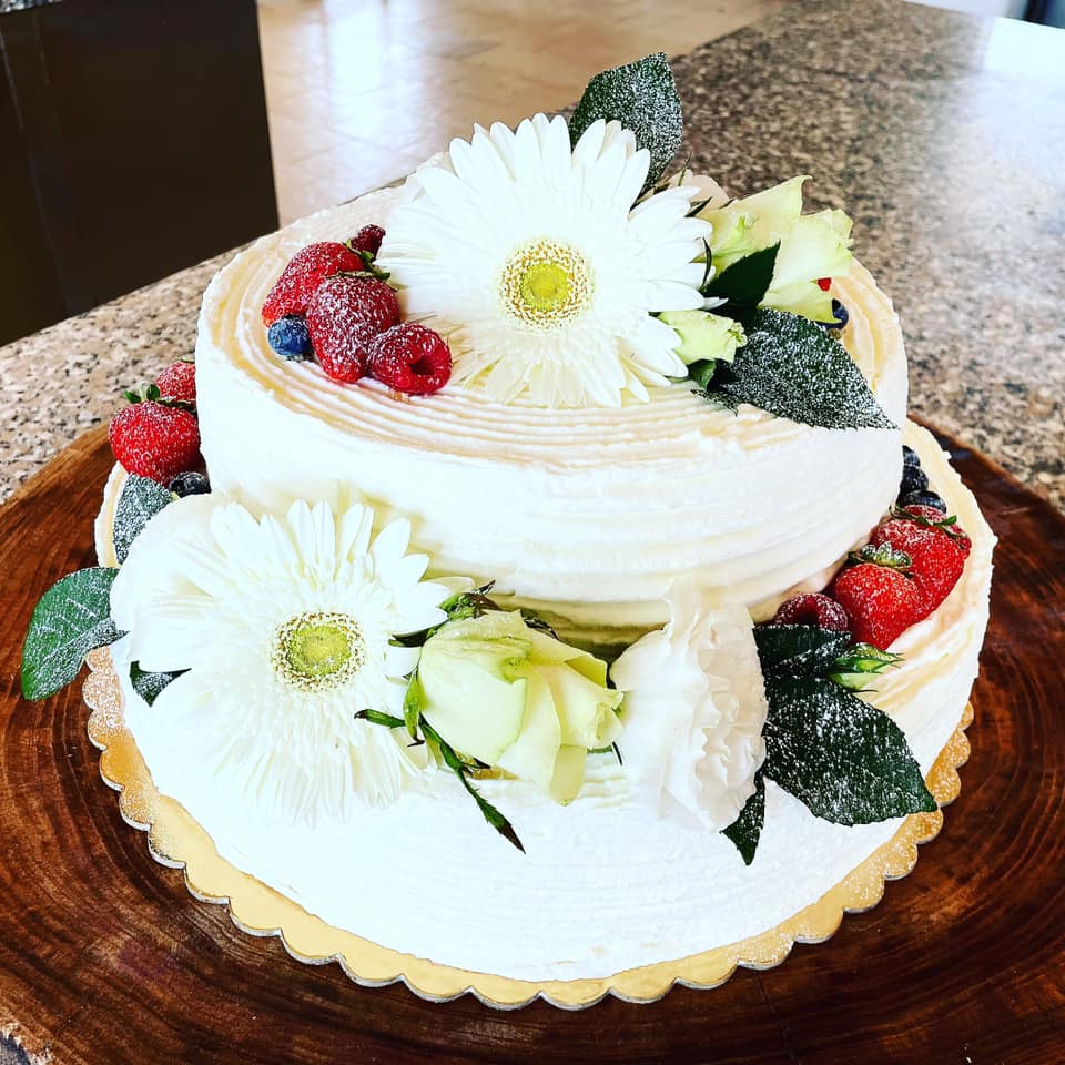 torta nuziale a due strati con fiori bianchi e frutti di bosco
