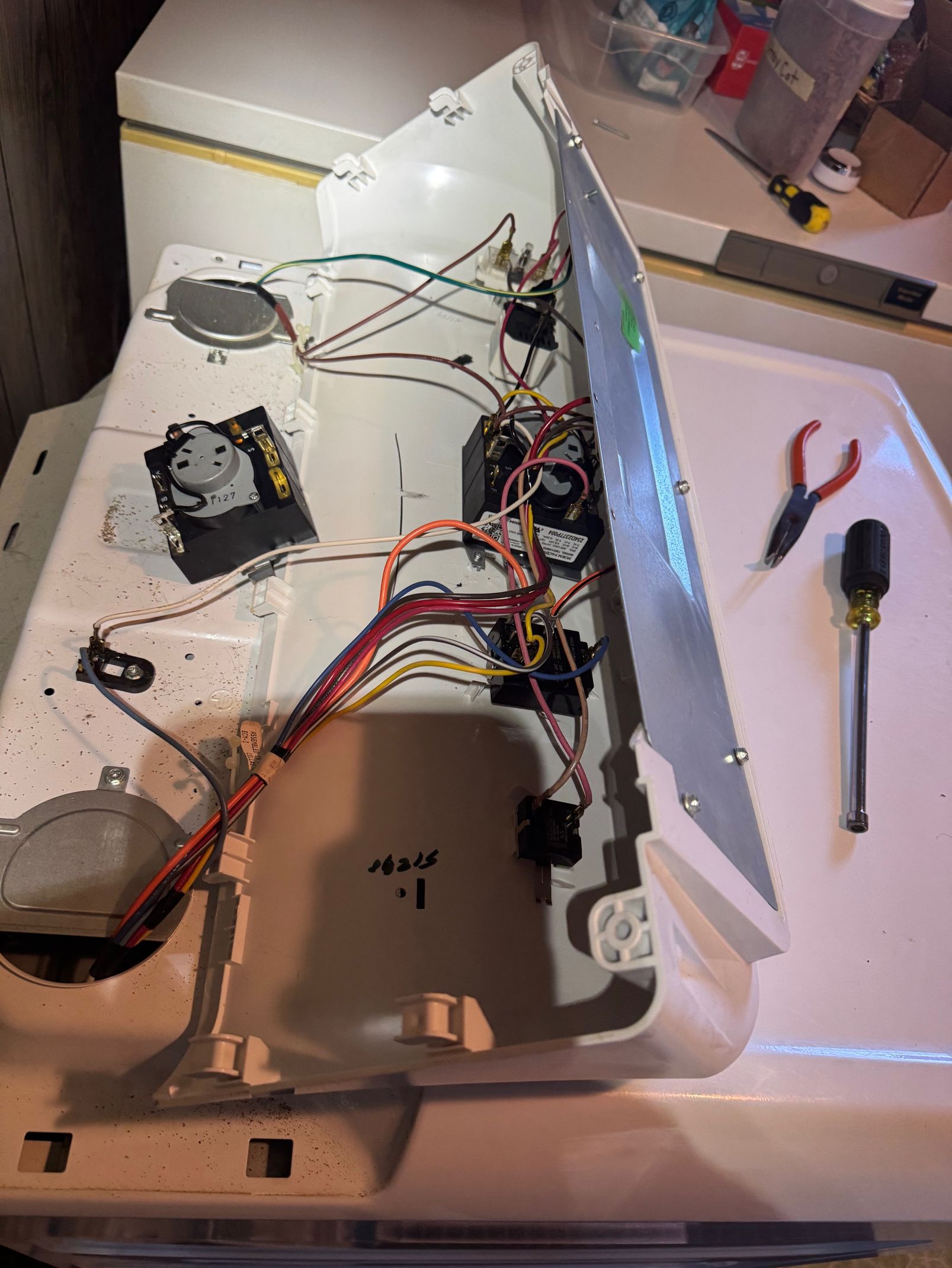 Washing machine's interior with wires, components, and tools, indicating repair or maintenance.