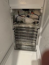 Interior of a refrigerator with a heavily frosted evaporator coil. Wires and electrical components are visible above the coil.
