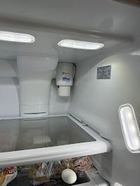 Interior of a white refrigerator with lighting.  A water filter is installed. A glass shelf and food are visible.