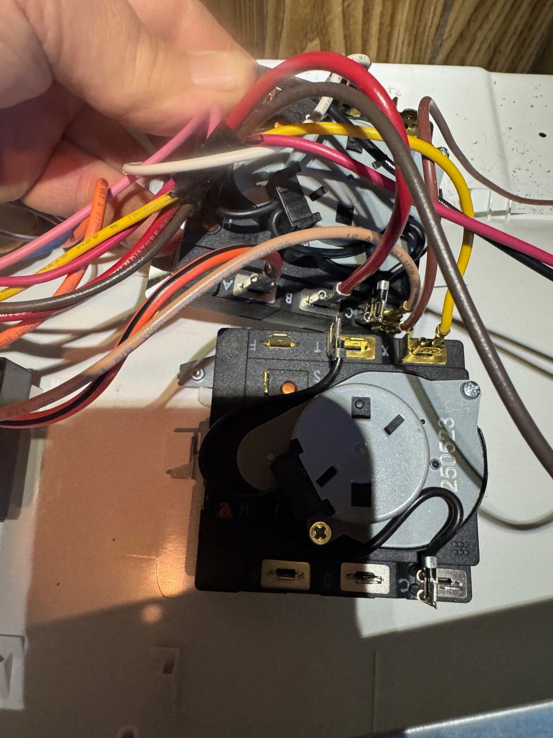 A hand holding wires connected to a black timer with various colored wires in a control panel.