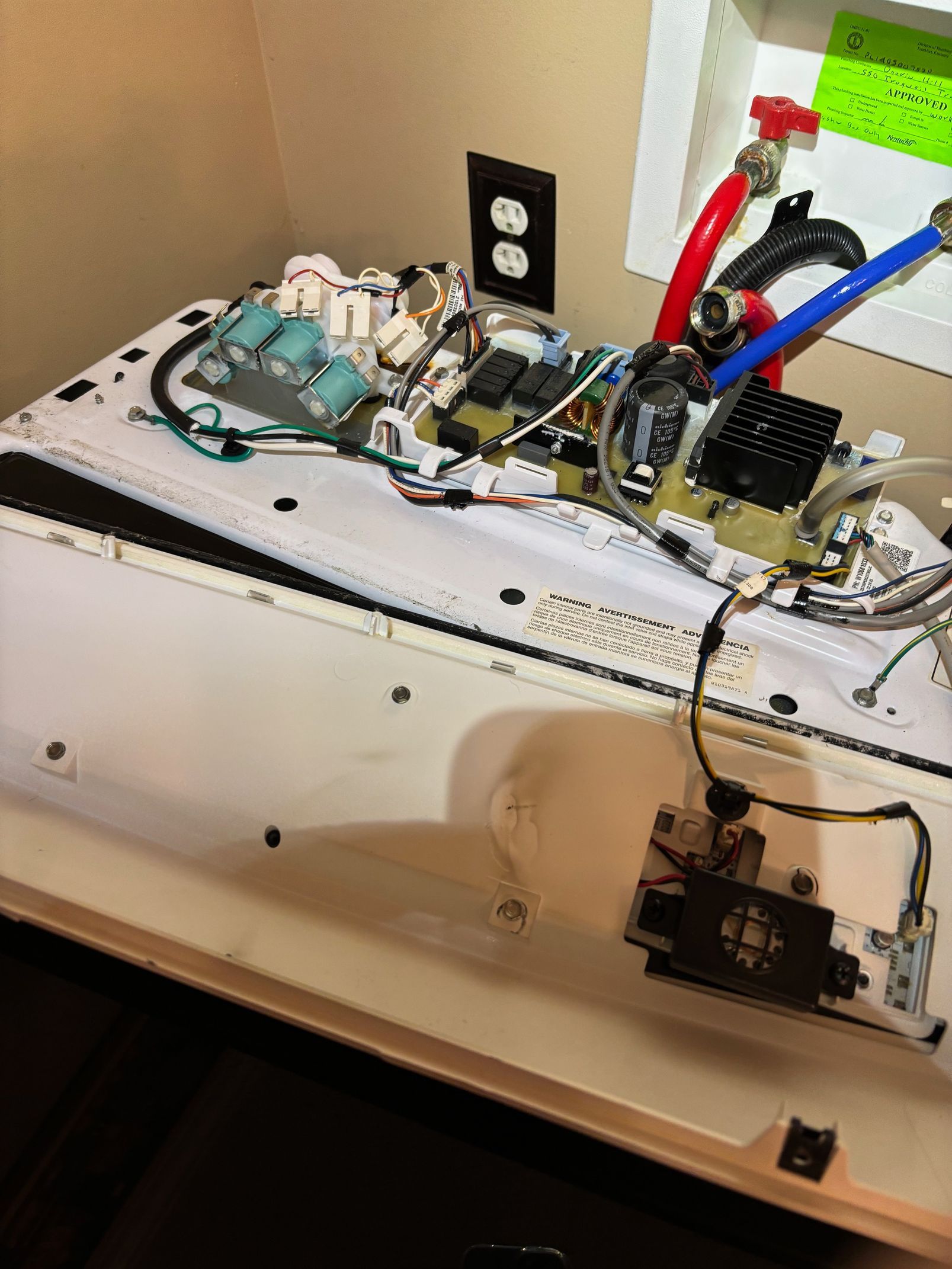 Open appliance with exposed interior components; wiring, circuit boards, and water pipes.