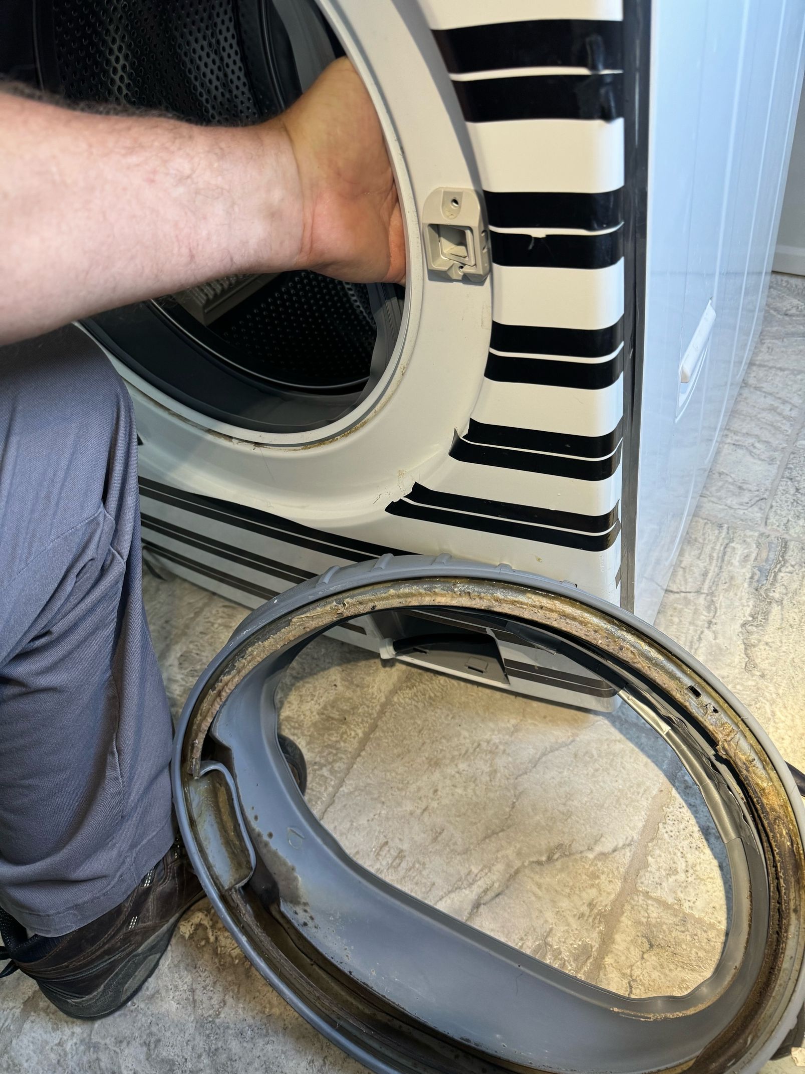 A person is kneeling down next to a washing machine with the door open.