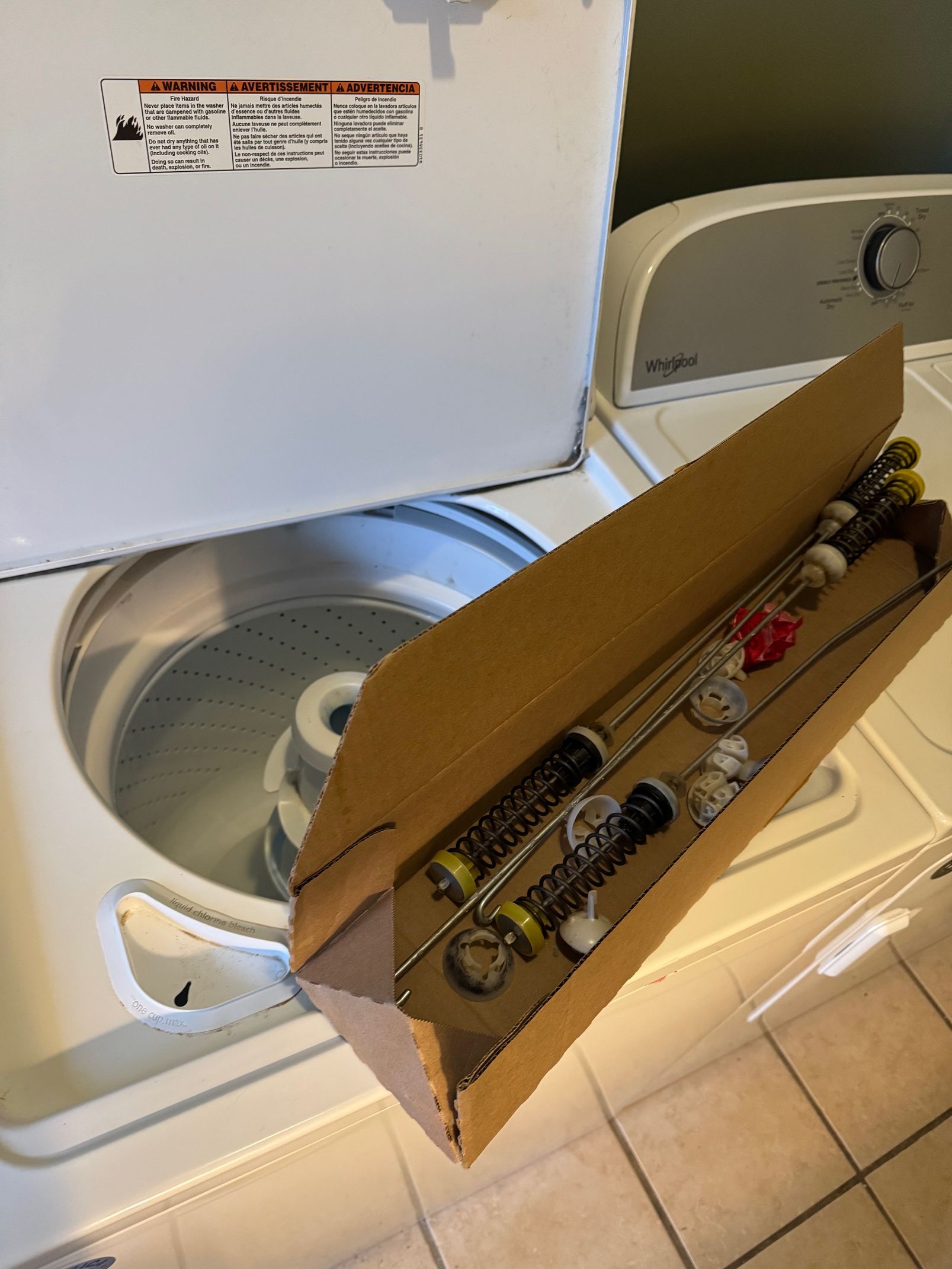 A washing machine with the lid open. A box of fishing poles sits in front.