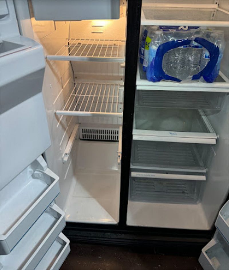Open, empty refrigerator with shelves; water bottles in the right door.