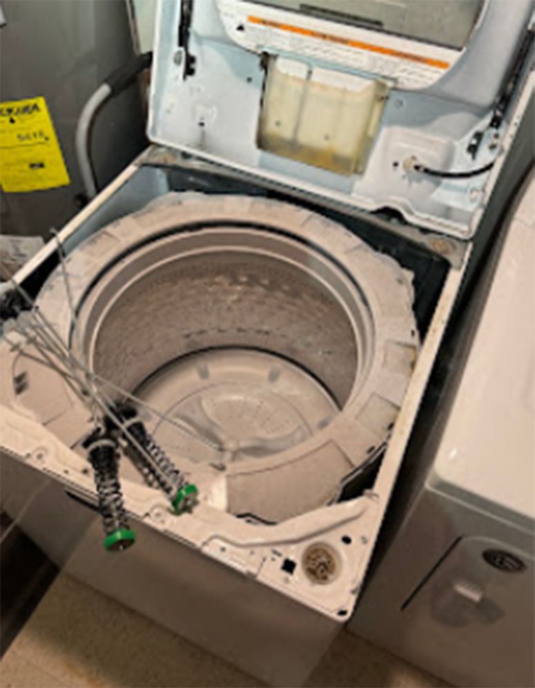 White washing machine with open top, revealing interior components and parts.