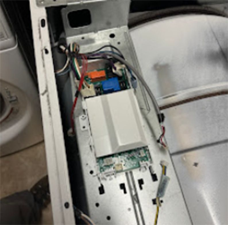 Interior view of a dryer's control panel, showing circuit boards, wiring, and a white plastic housing.