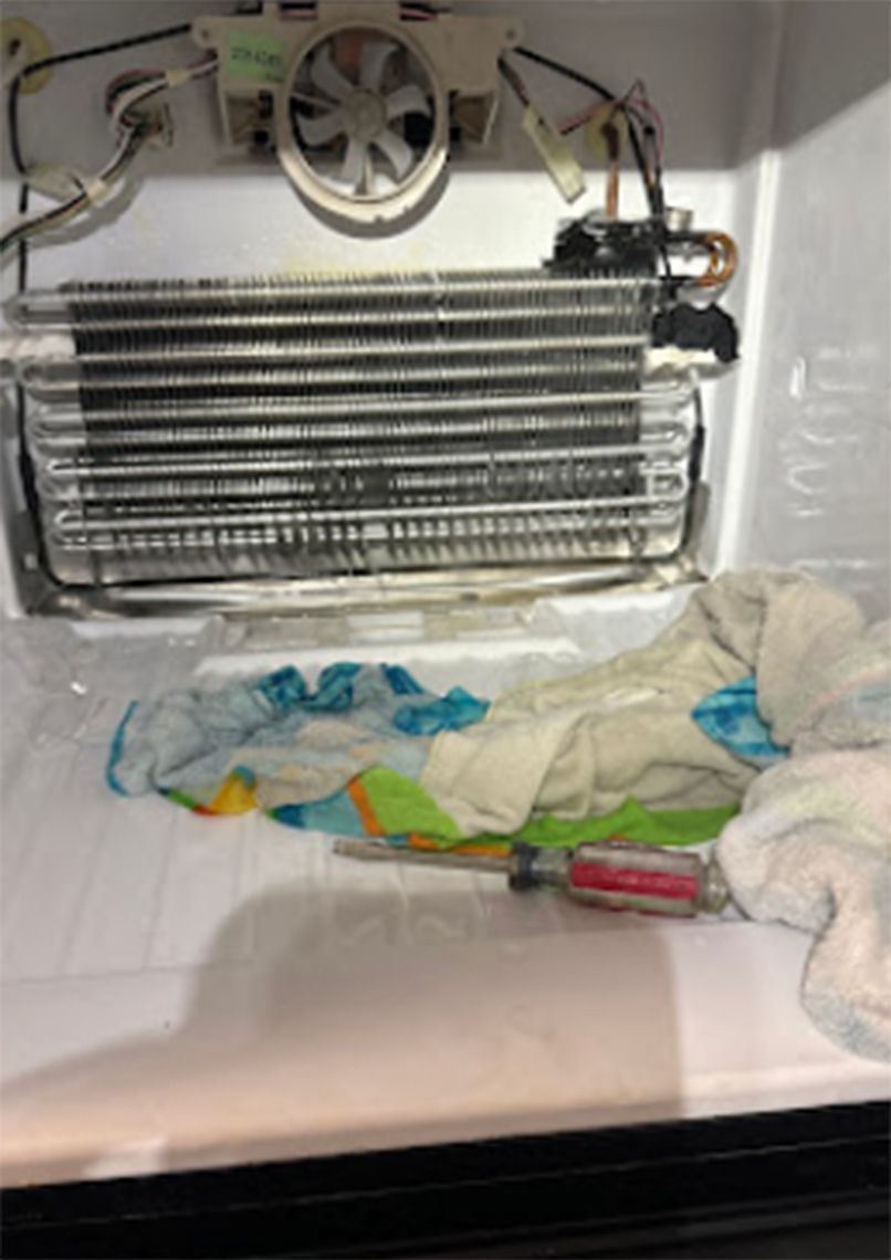 Refrigerator freezer interior with icy coils and fan. Tidy, folded cloths and a screwdriver are on the bottom shelf.
