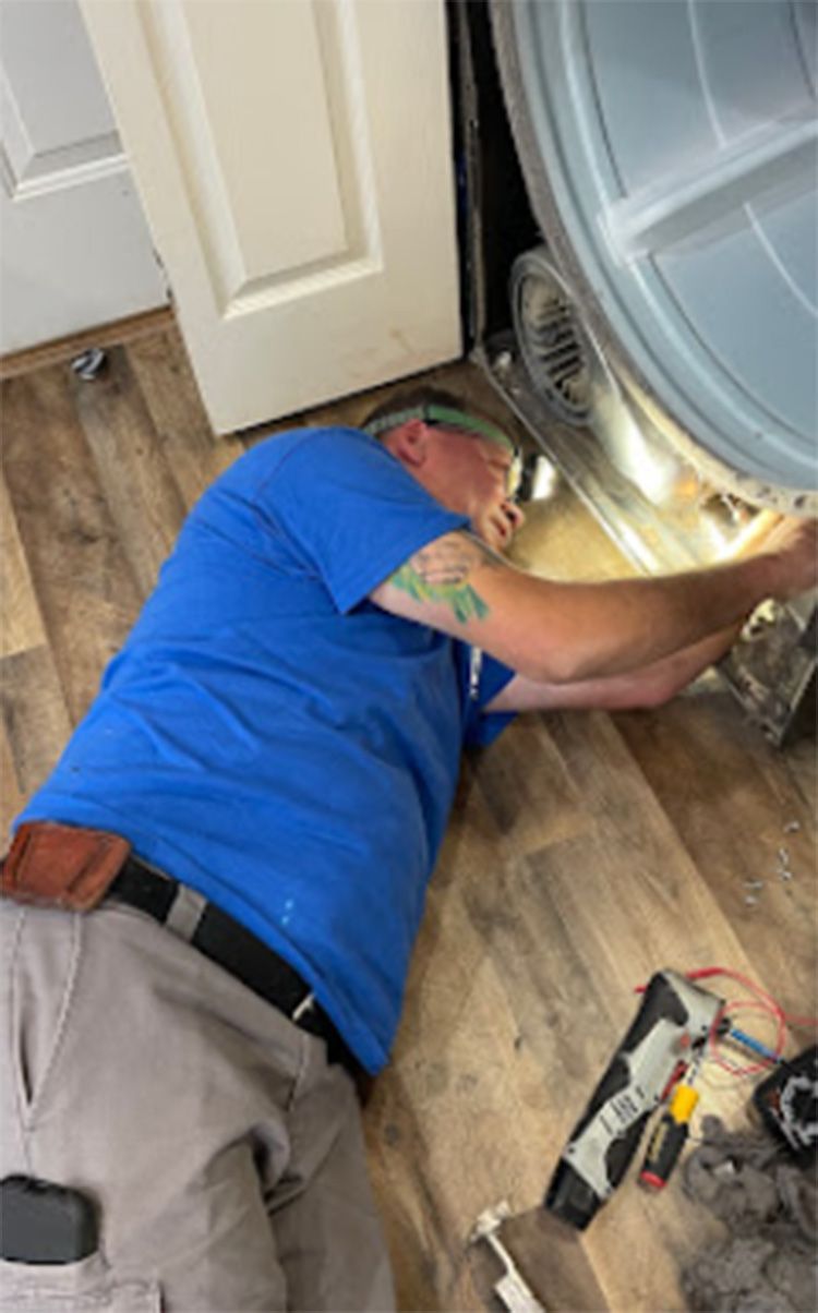 Man in blue shirt works on a dryer, lying on floor with tools.