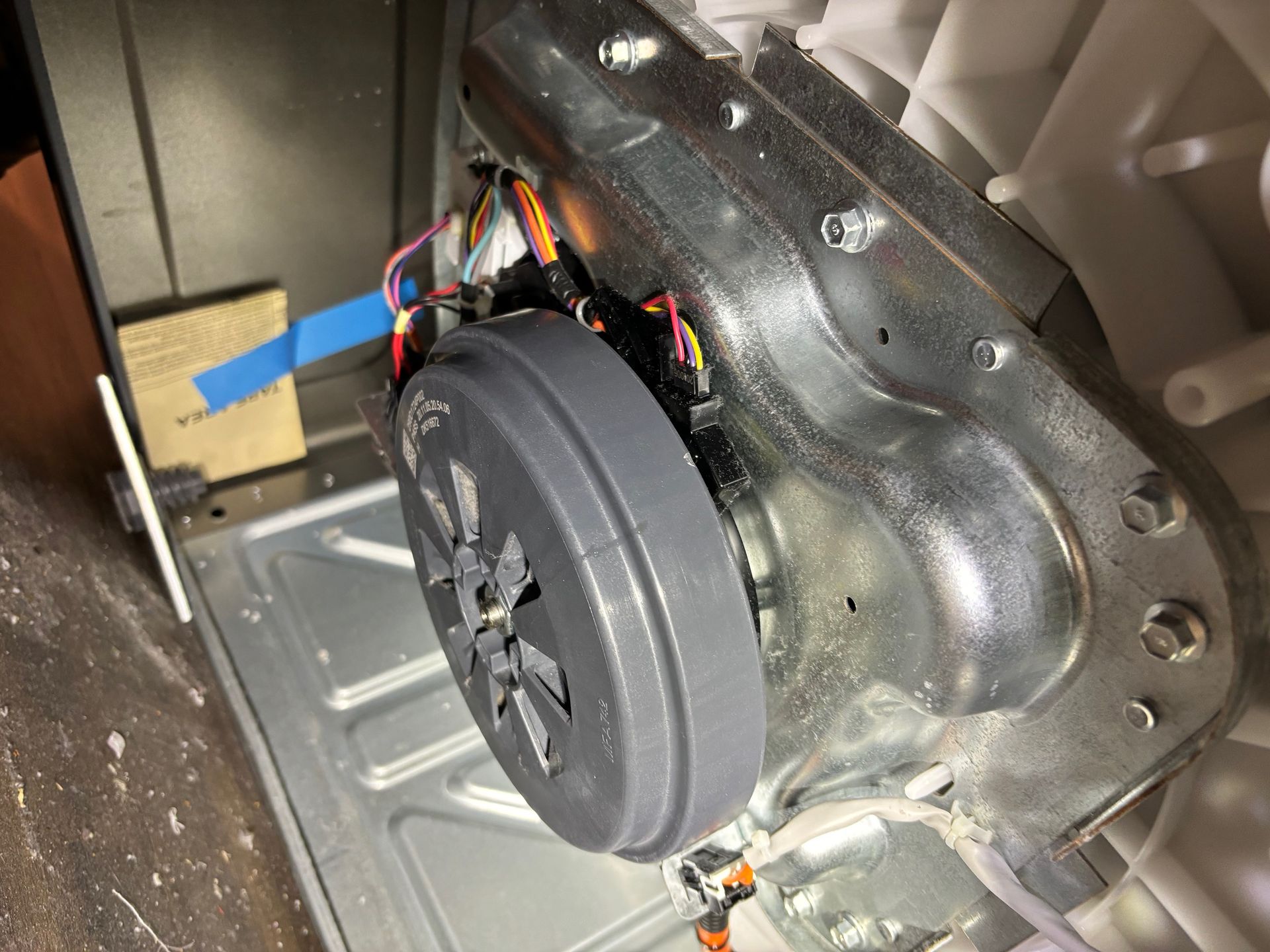 Washing machine motor and pulley inside the appliance. Gray metal housing, wires, and dark gray motor.