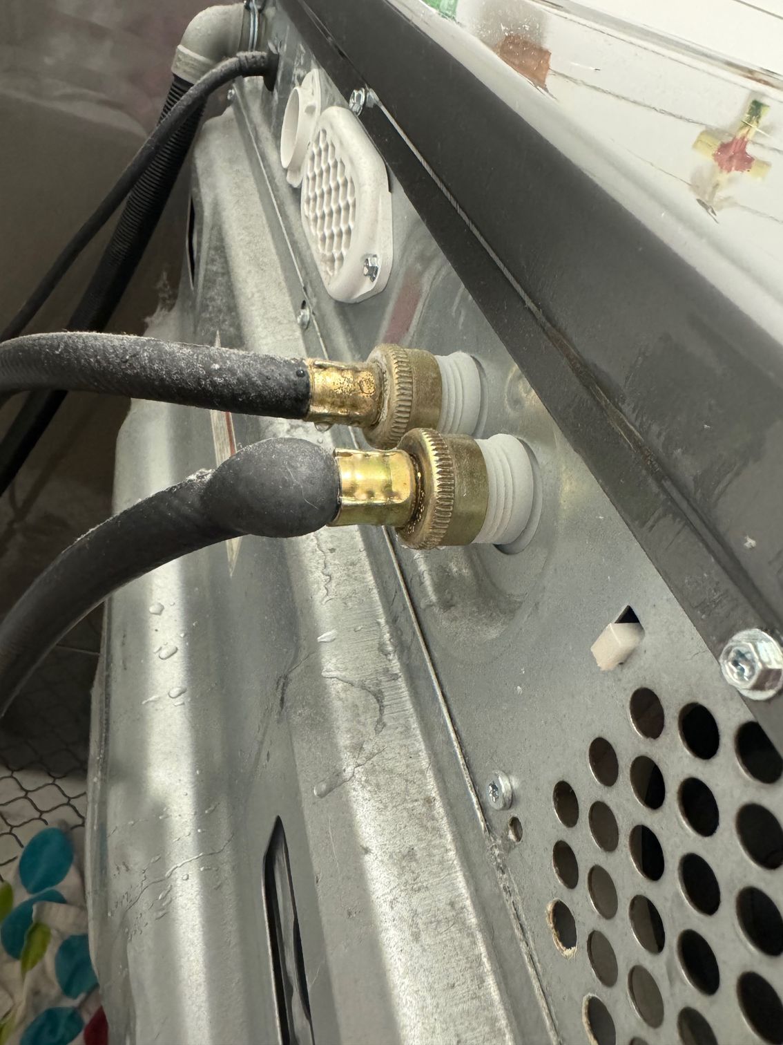 Close-up of washing machine water inlet. Two hoses attached to brass fittings on the back of the machine.