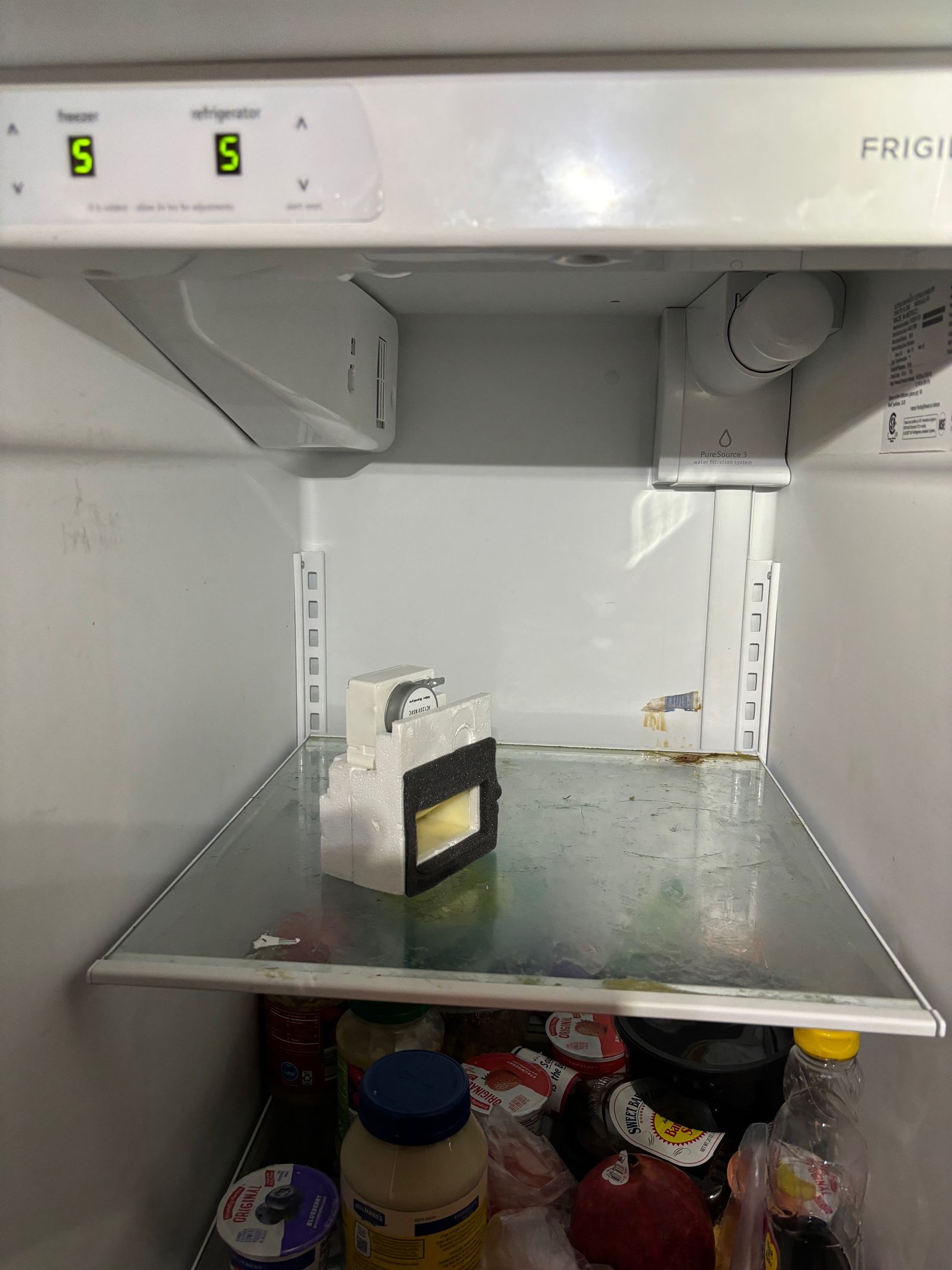 Open refrigerator interior; shelf with ice maker and controls.