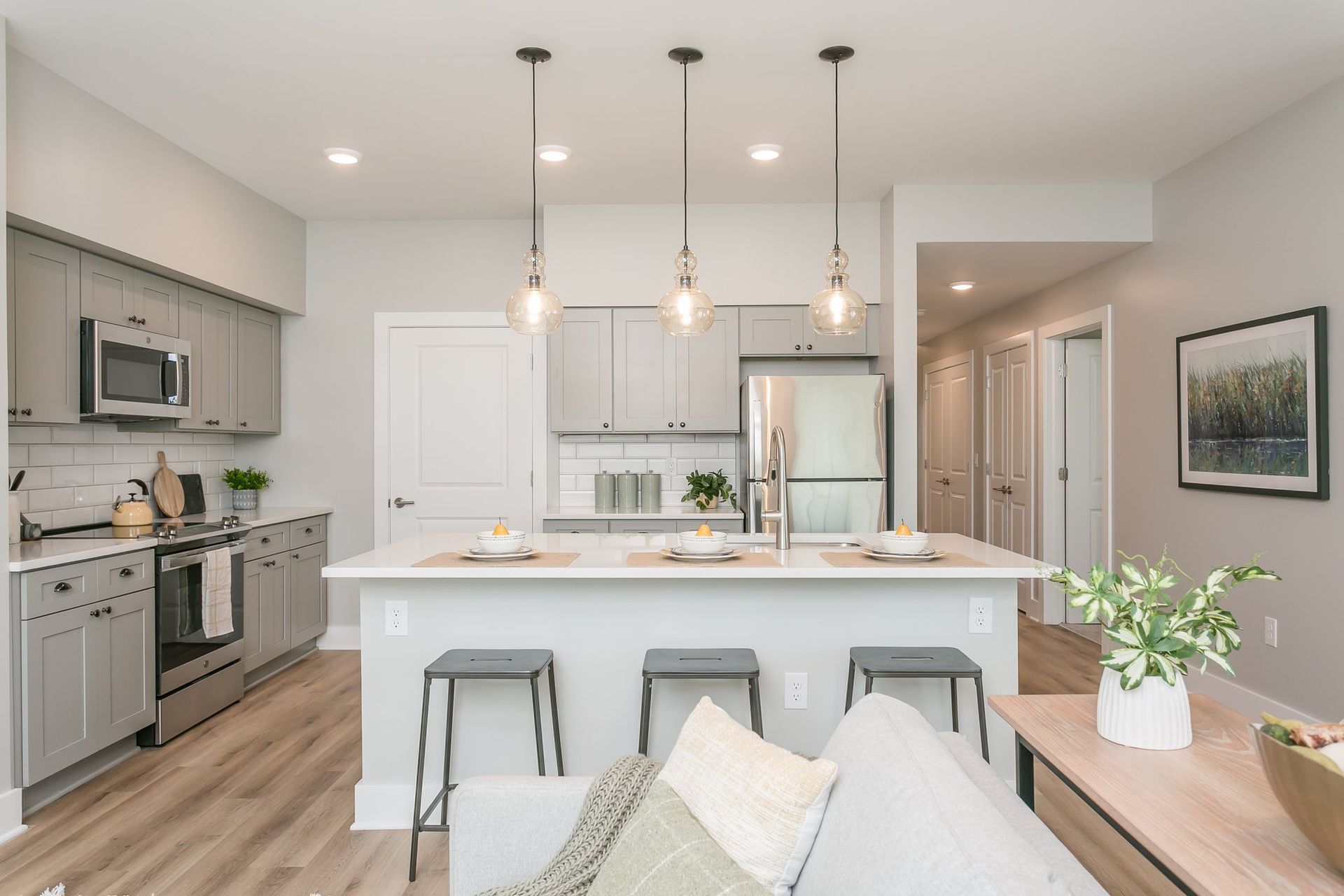 Modern kitchen with gray cabinets, island with stools, and stainless steel appliances, open to a living space.