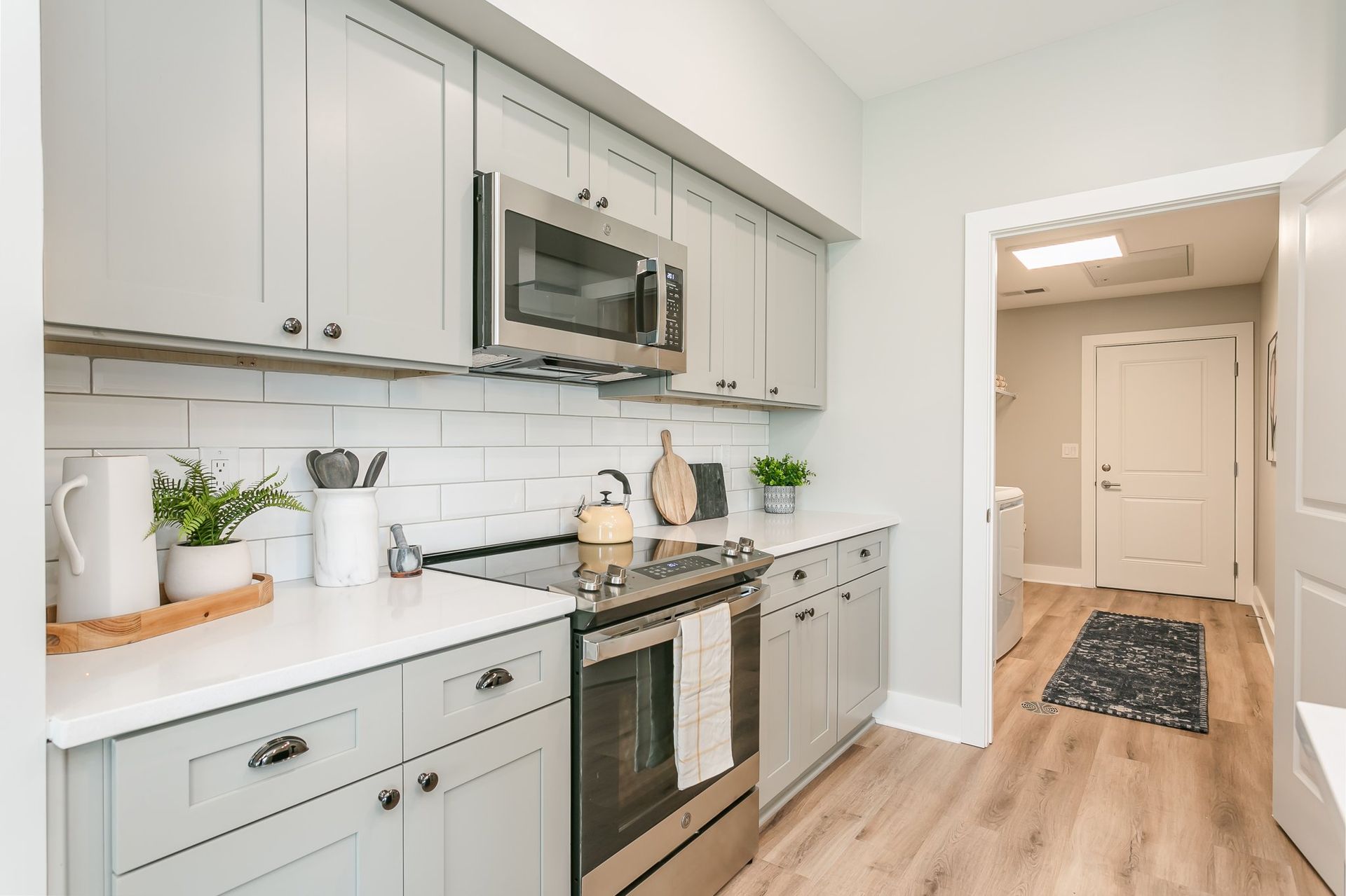 A modern kitchen with gray cabinets, white countertops, and stainless steel appliances. A doorway leads to a bathroom.