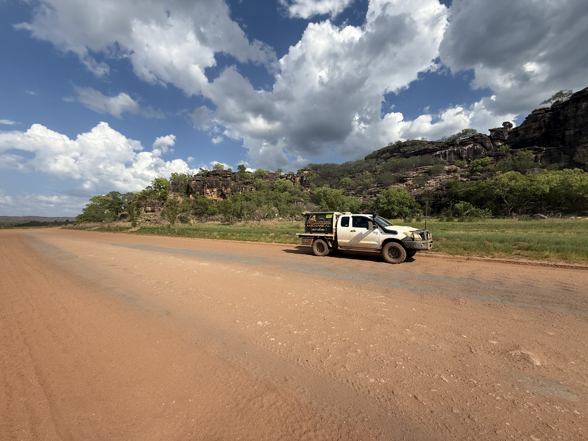 White truck parked on a dirt road next to grassy terrain, with rocky hills and a cloudy blue sky — Full Noise Mechanical in Humpty Doo, NT