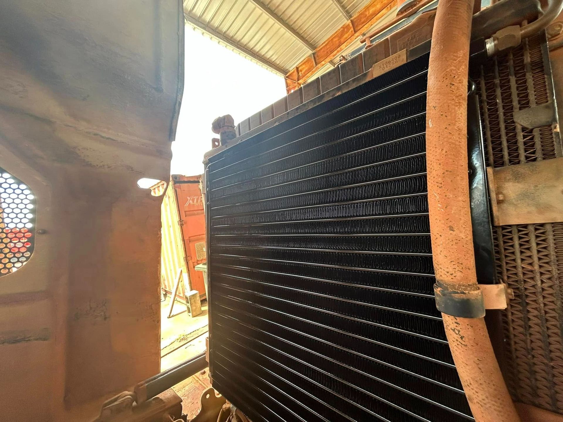 Black radiator in a machine, with a tan hose attached. Bright light shines from above — Full Noise Mechanical in Humpty Doo, NT