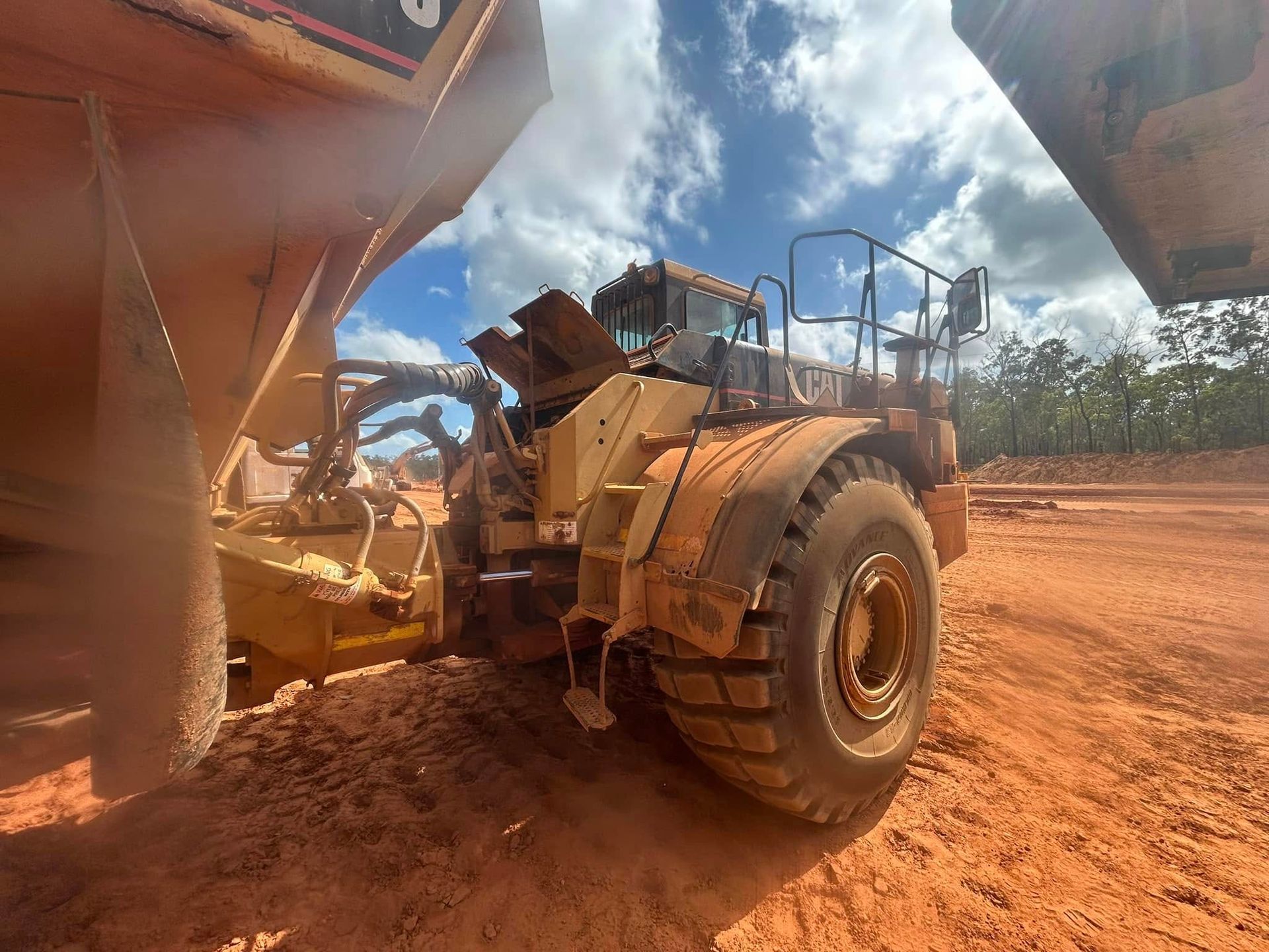 Yellow mining truck in a dirt area, with a second truck visible on the right, under a blue sky — Full Noise Mechanical in Humpty Doo, NT
