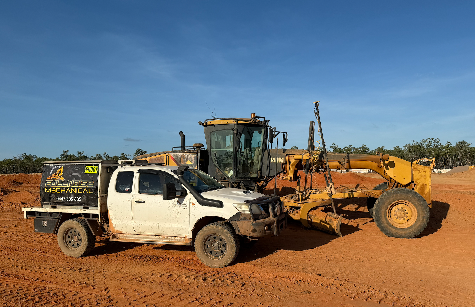 A white pickup truck and yellow grader sit on red dirt under a blue sky — Full Noise Mechanical in Humpty Doo, NT