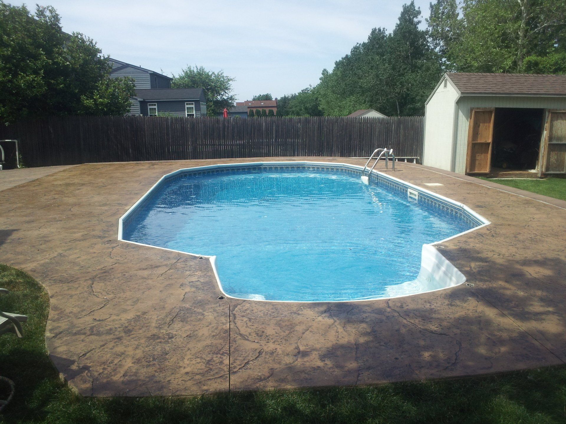 A large swimming pool in a backyard with a shed in the background