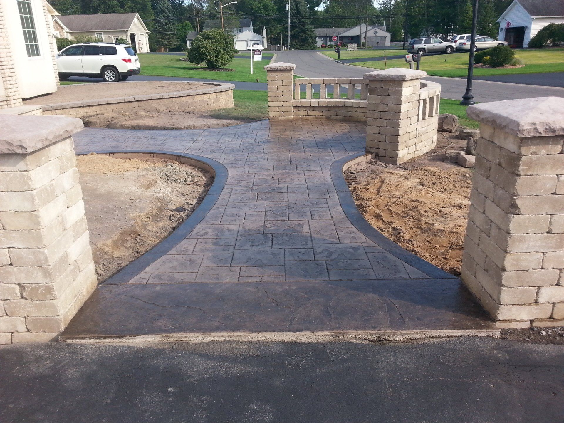 A brick walkway leading to a house with a white suv parked in the background