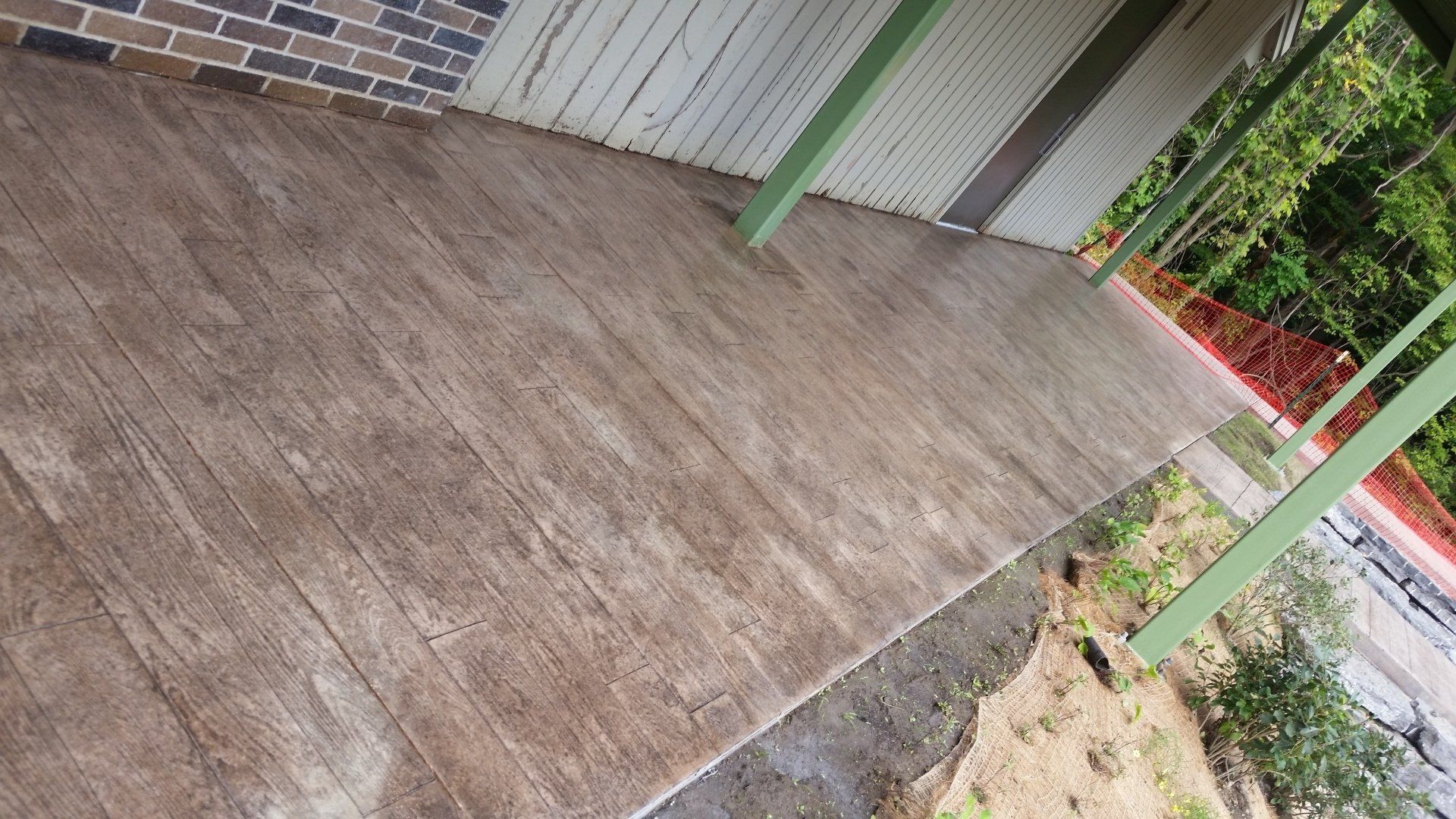 A concrete walkway leading to a house with a brick wall.