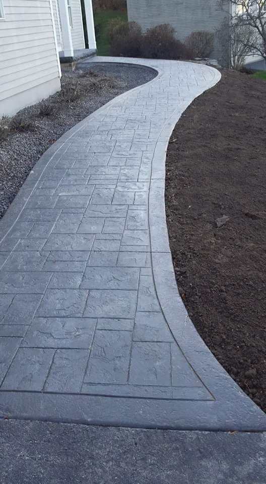 A concrete walkway leading to a house with a house in the background.