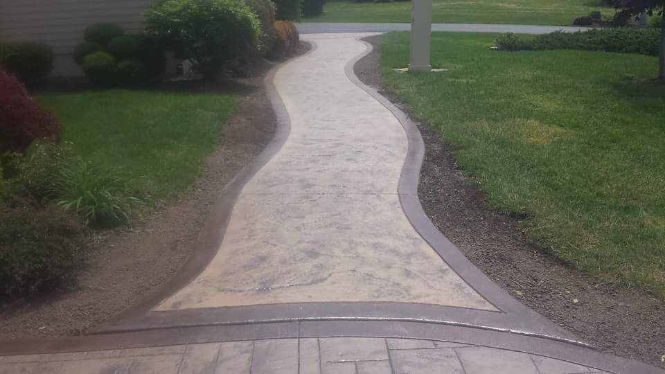A concrete walkway going through a lush green yard.