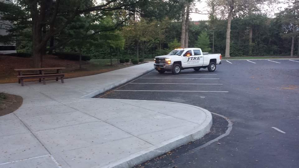 A white truck is parked in a parking lot next to a sidewalk.