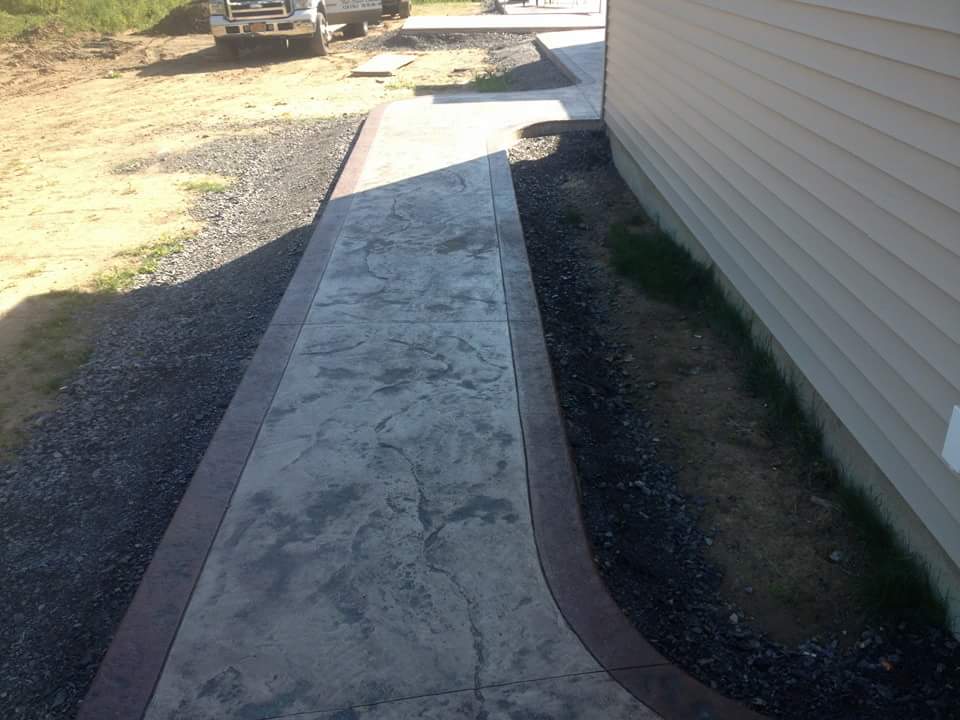 A concrete walkway leading to a house with a truck parked in the background