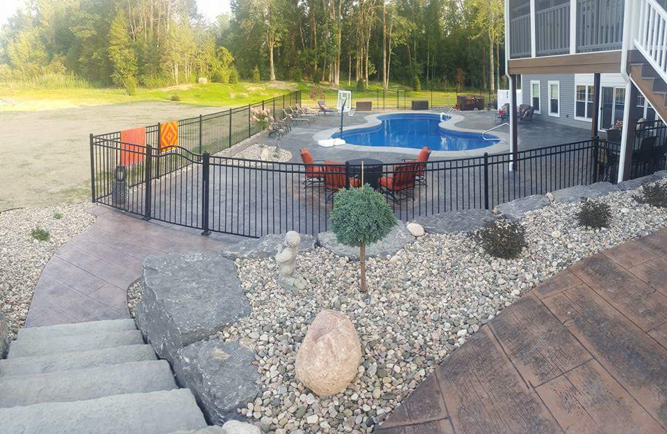 A fence surrounds a large swimming pool in a backyard.