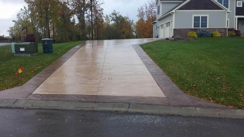 A concrete driveway leading to a house on a rainy day.
