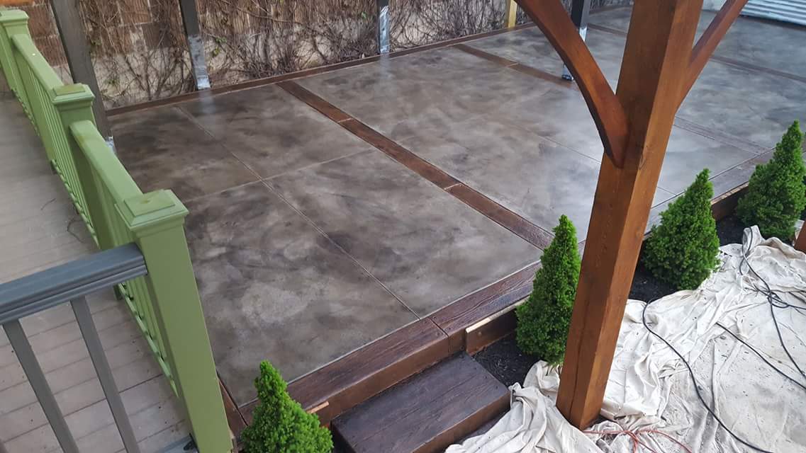 A concrete patio with a green railing and a wooden pergola.