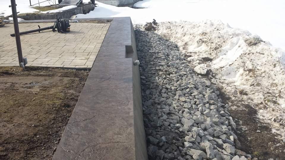A concrete wall is surrounded by gravel and snow.