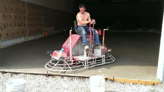 A man is riding a concrete trowel on a concrete floor.